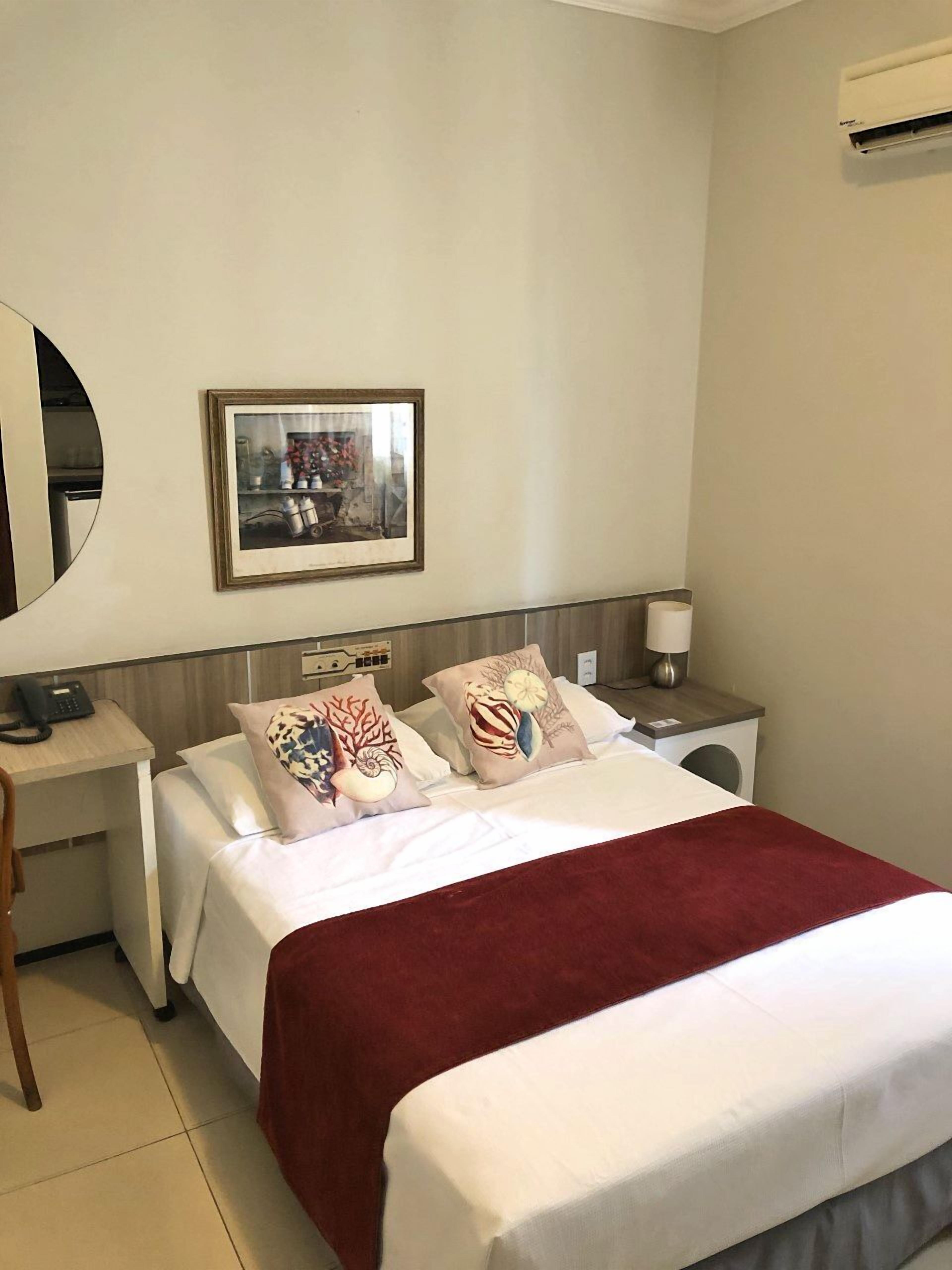 Une chambre d’hôtel avec un lit, une table de chevet avec une lampe, un miroir et un tableau encadré au mur.