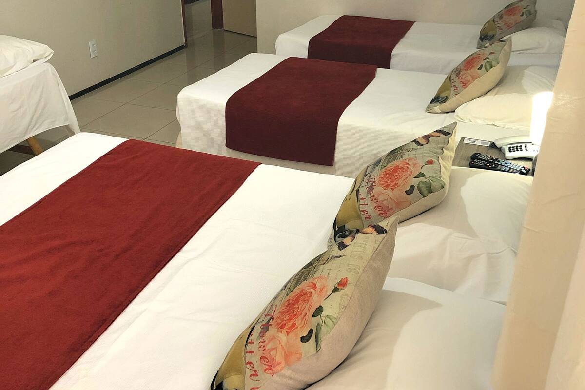 A hotel room with three beds, each with white linens and red bedspreads. There are floral-patterned pillows on the beds.