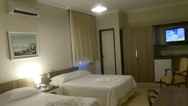 Una habitación de hotel con dos camas, un escritorio, una silla, un televisor y un cuadro en la pared.