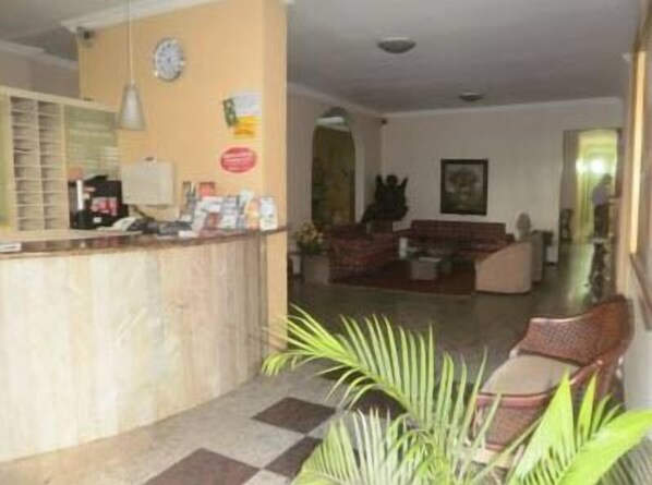 Un área de recepción con mostrador, un reloj y una zona de estar con sofá y sillones.