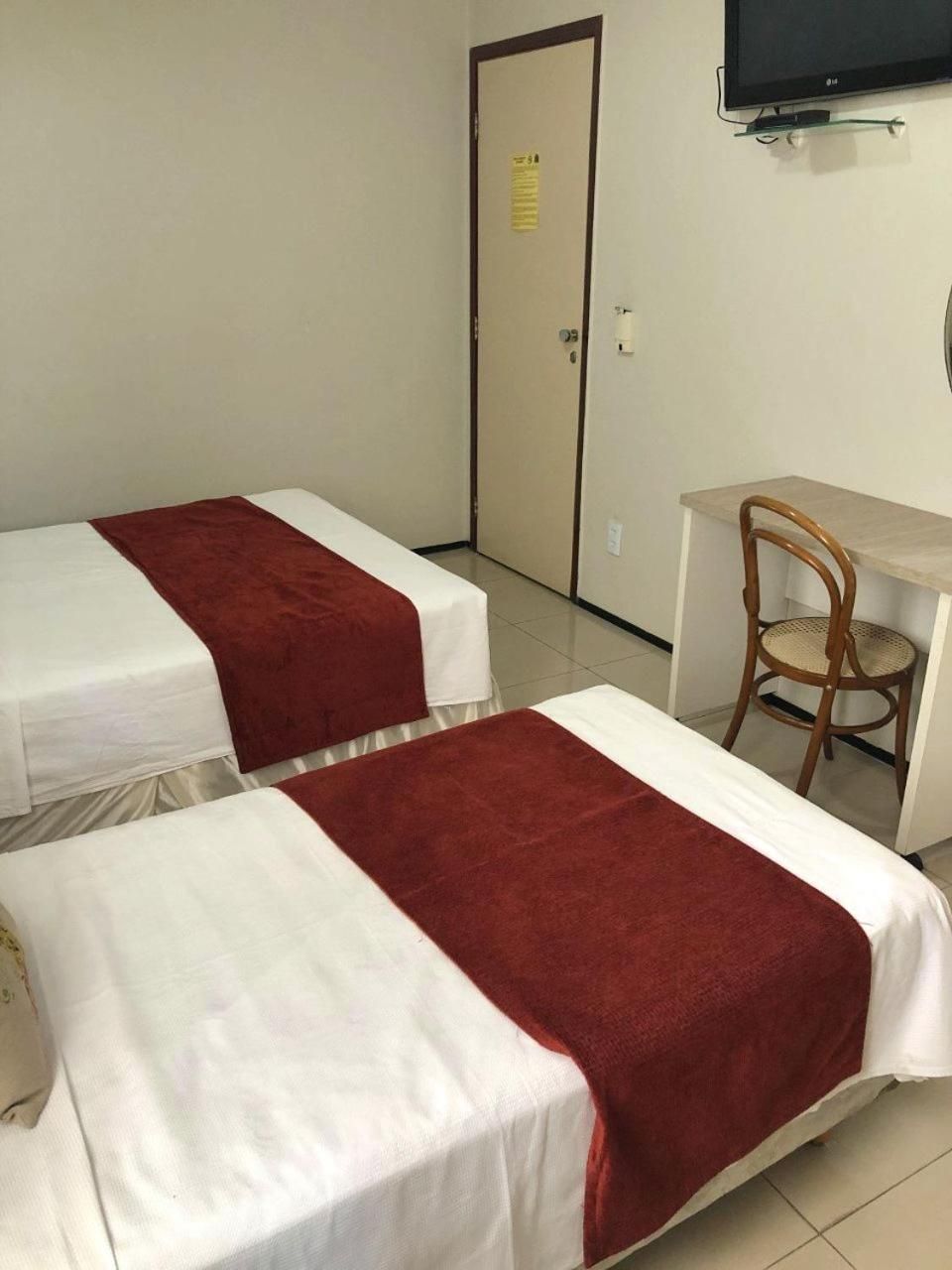 A hotel room with two beds, a desk, a chair, and a television.