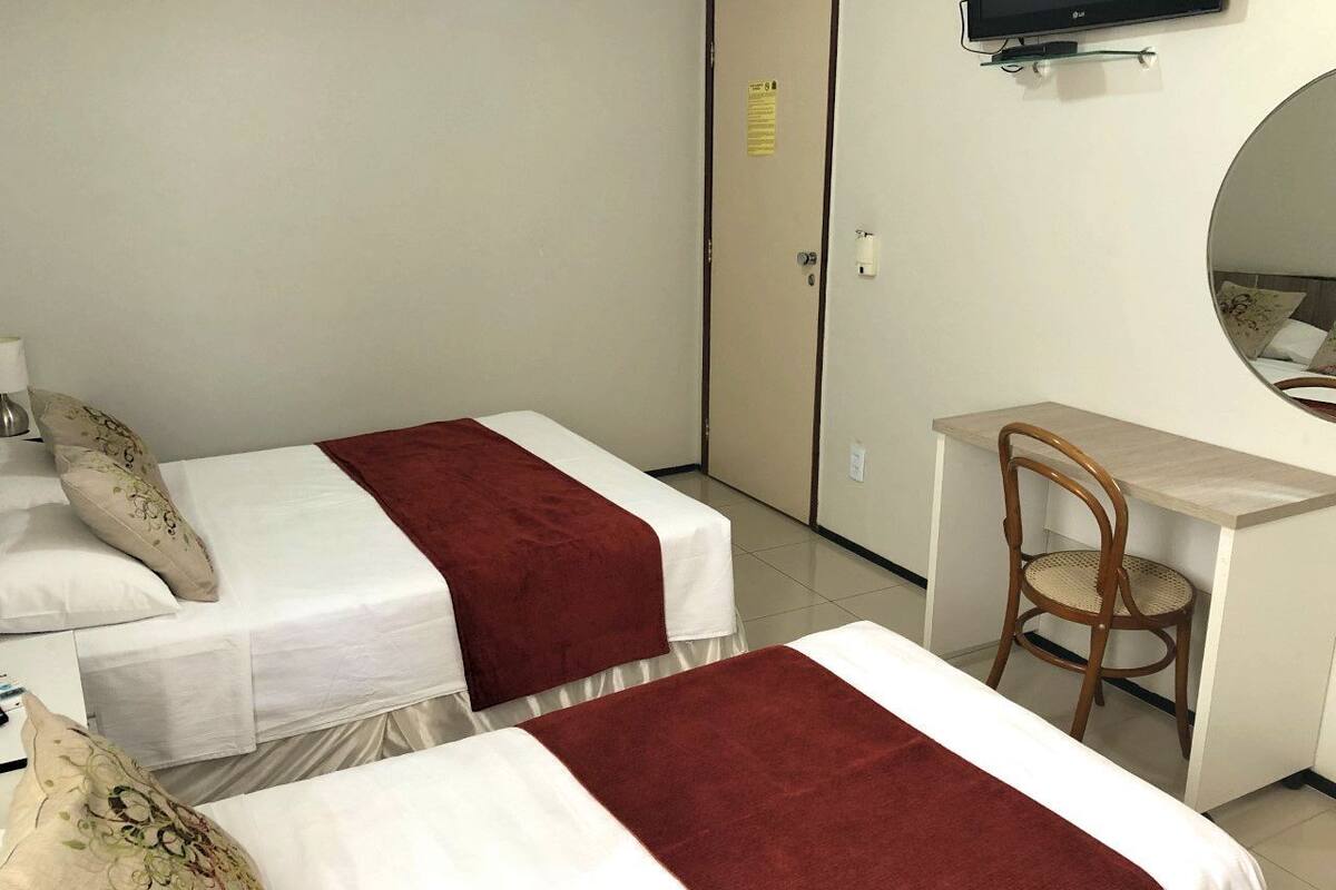 A hotel room with two beds, a desk, a chair, a television, and a door with a sign.