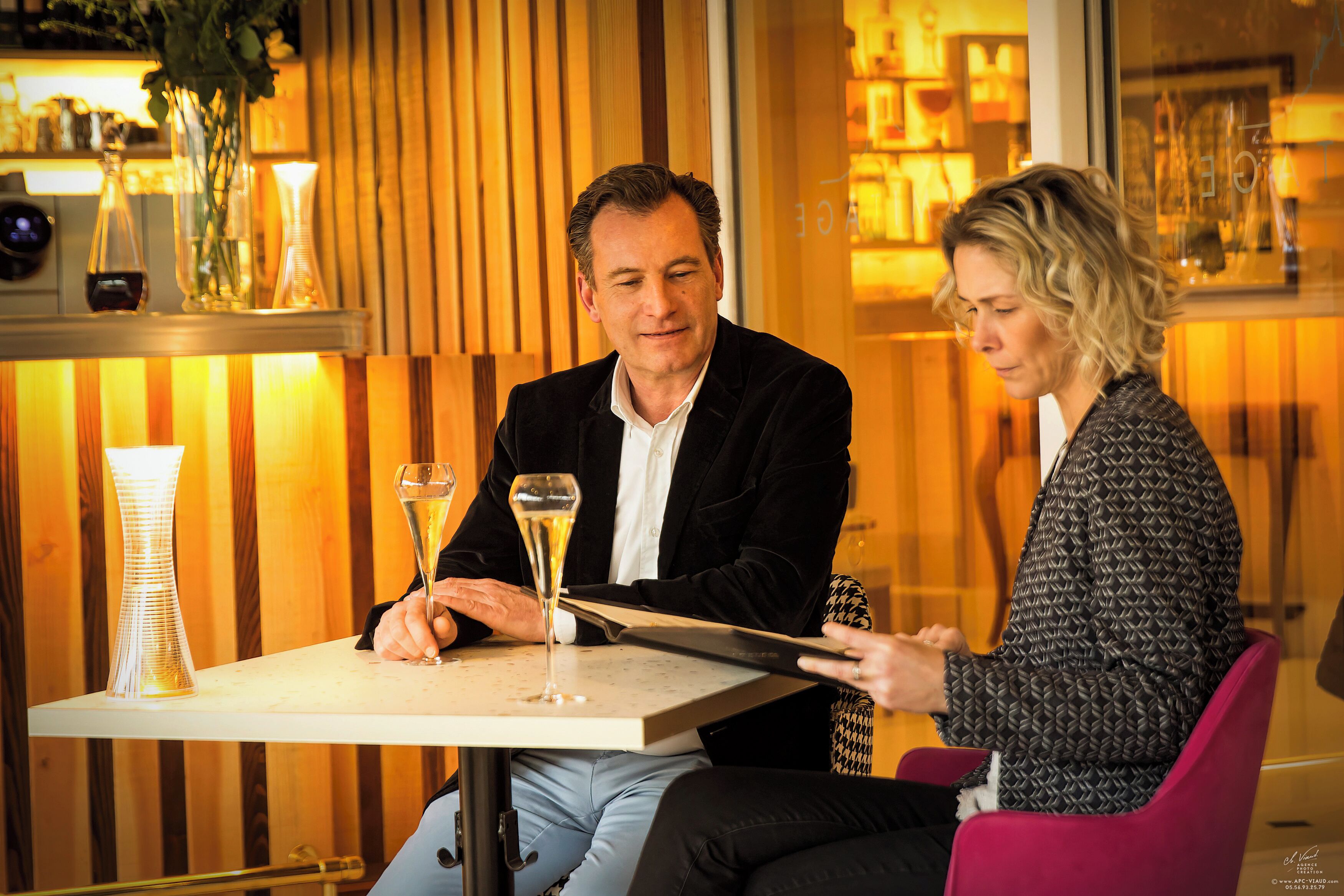 Zwei Personen sitzen an einem Tisch mit einer Champagnerflasche und Gläsern.