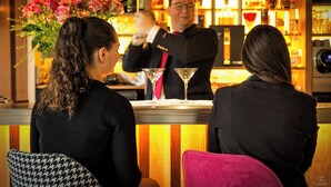 Een bar met een barman, twee gasten die zitten en een toog met flessen en glazen.