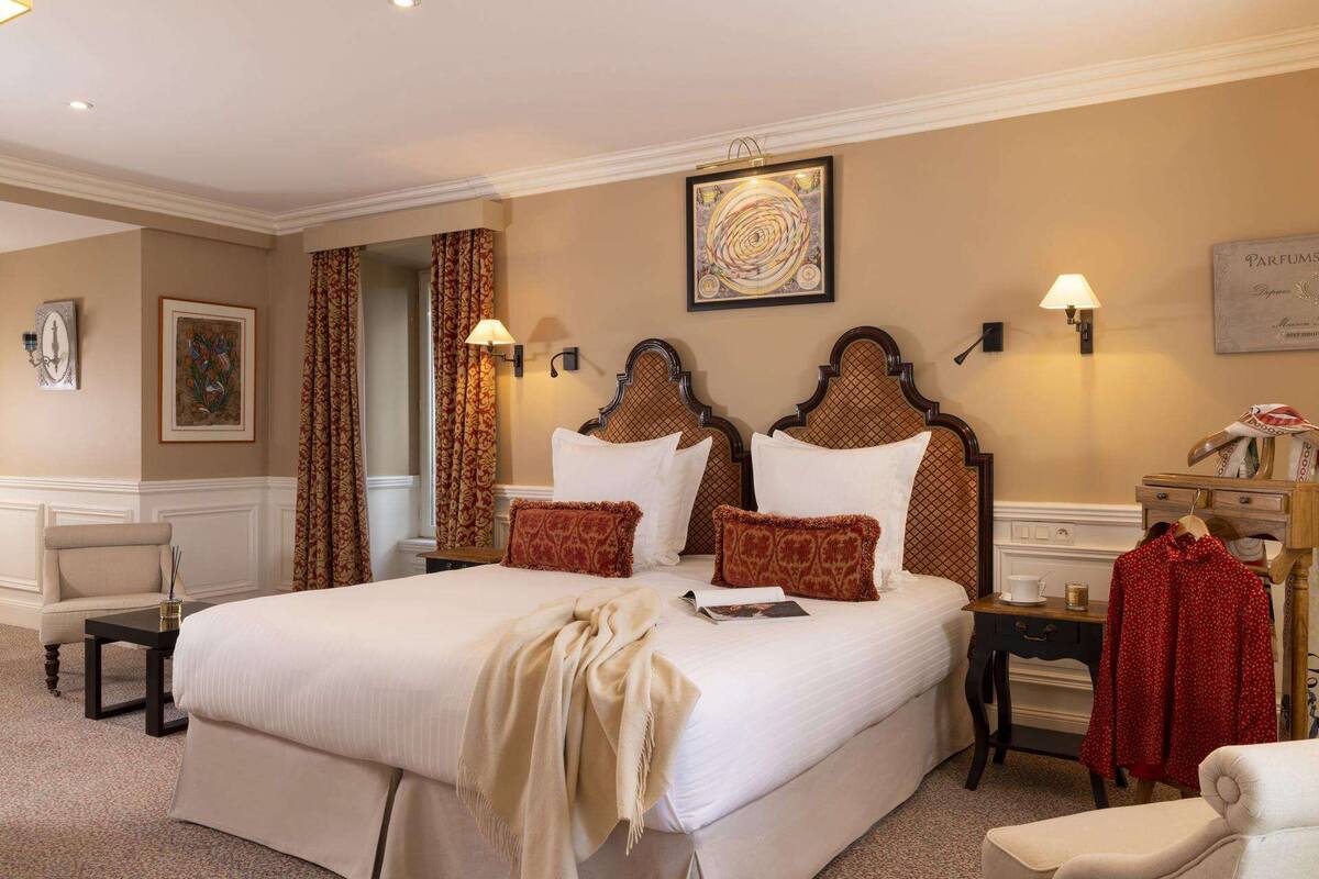 Ein Hotelzimmer mit einem großen Bett, zwei Nachttischen, einem Sessel, einer Lampe und einem gerahmten Kunstwerk an der Wand.