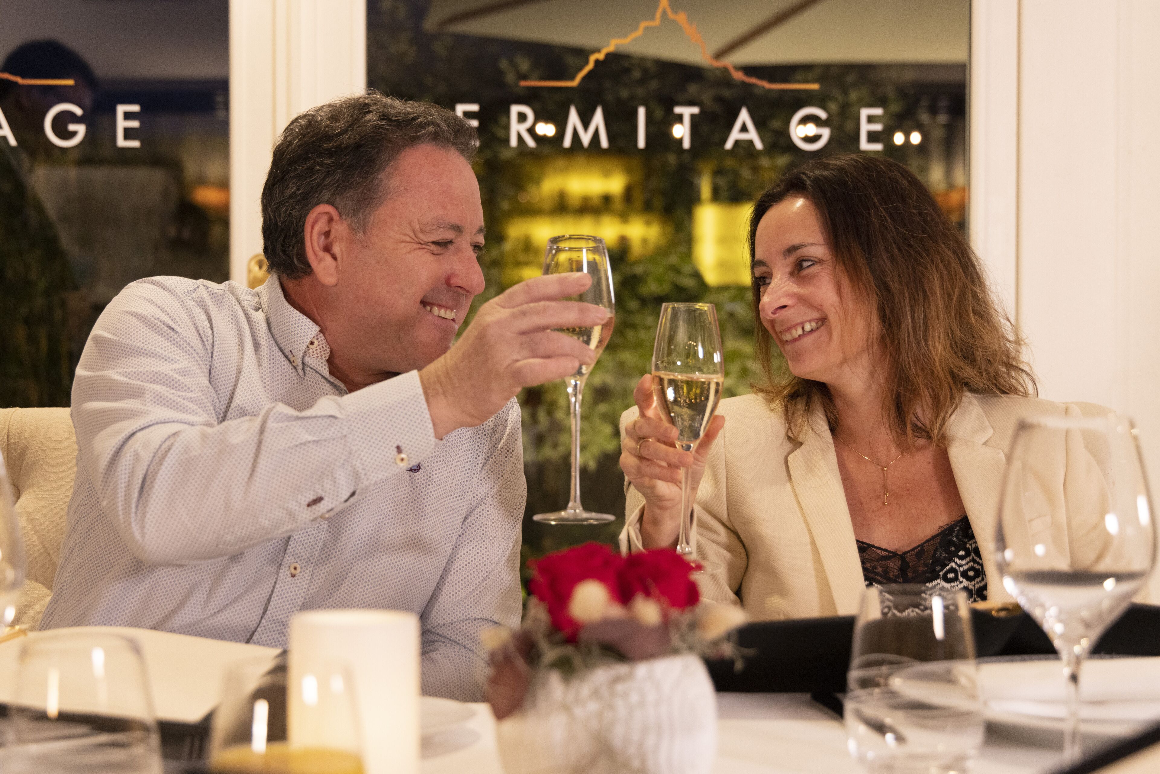 A man and a woman toasting with wine glasses at a table with a floral centerpiece.