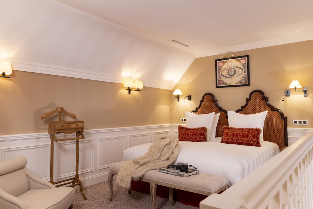 Ein Schlafzimmer mit einem großen Bett, Nachttischlampen, einem hölzernen Nachttisch, einem Kleiderhaken und einem gerahmten Bild an der Wand.