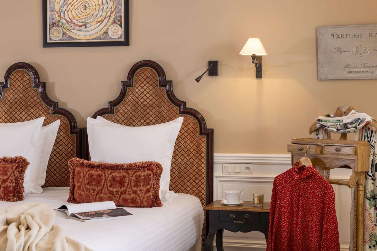 Een hotelkamer met een bed, nachtkastje, lamp, ingelijst schilderij en een houten dressoir.