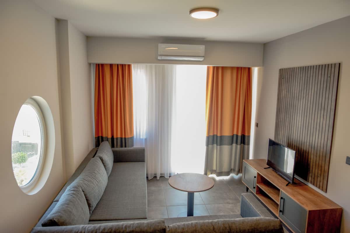 A modern living room with a sofa, a round coffee table, a TV on a wooden stand, and a large window with curtains.
