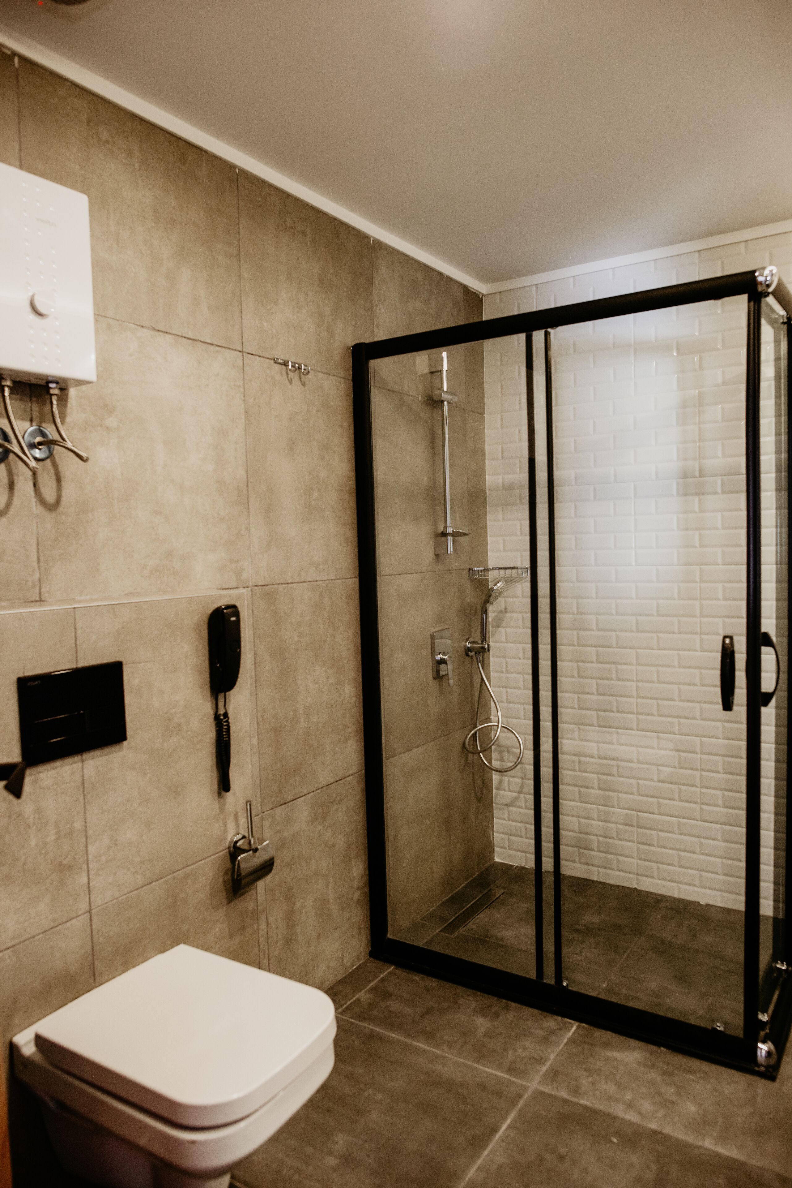 A bathroom with a glass-enclosed shower, a toilet, and a wall-mounted telephone.