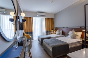 Habitación de hotel con dos camas, un escritorio, una silla, un espejo grande y una ventana con cortinas.
