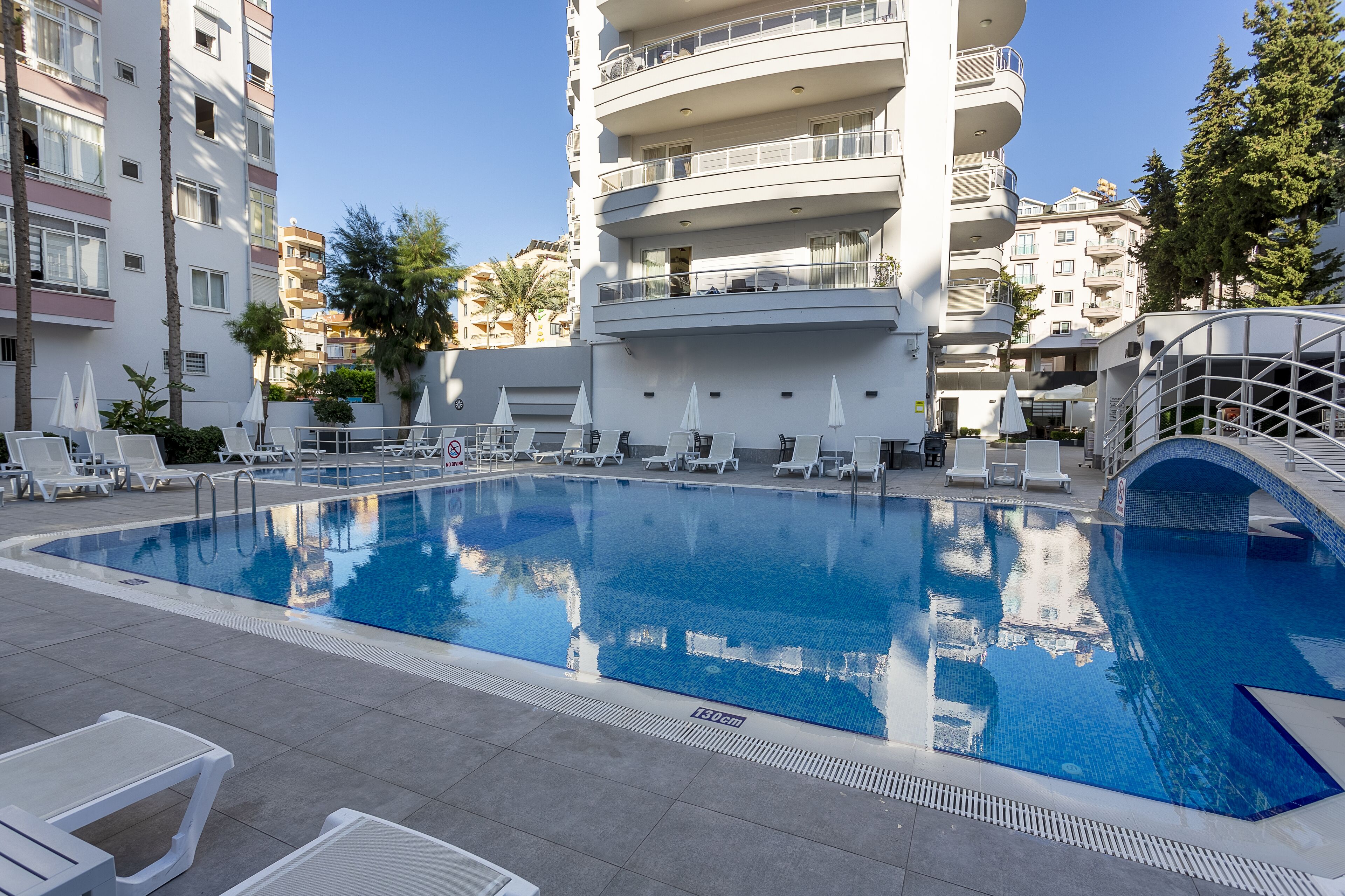 A swimming pool with lounge chairs and umbrellas, surrounded by multi-story buildings.