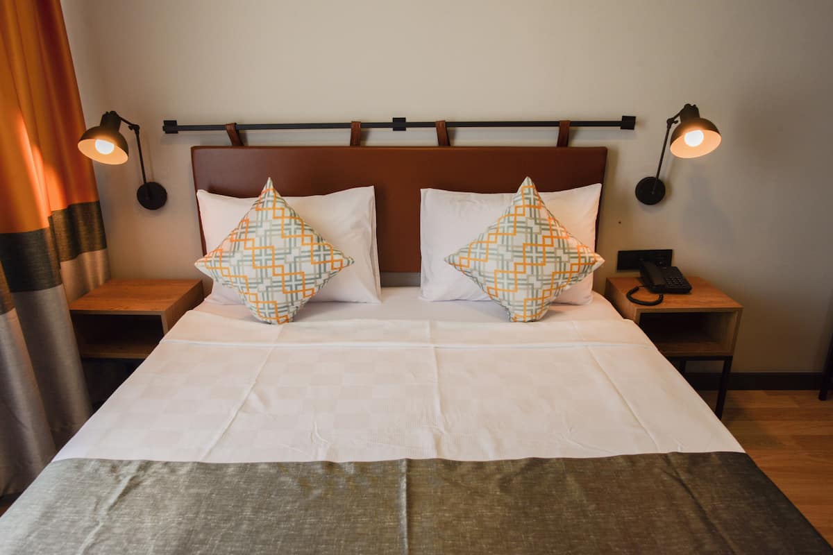 A neatly made bed with two pillows, a headboard, two bedside tables with lamps, and a curtain.