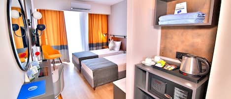 A hotel room with a bed, a desk with a kettle, a mirror, and a shelf with towels.