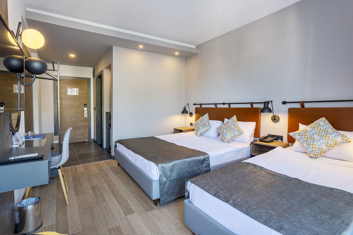 A hotel room with two beds, a desk, a chair, and a trash bin.