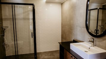 A modern bathroom with a glass shower enclosure, a white sink with a black countertop, and a mirror with a black frame.