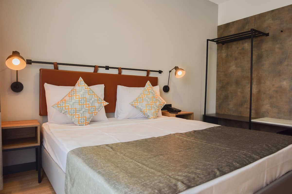 A neatly made bed with patterned pillows, a bedside table with a lamp, and a wall-mounted shelf.