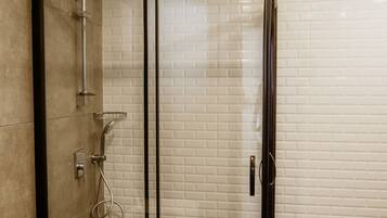 A glass-enclosed shower with a black frame, white tiled walls, and a concrete floor.