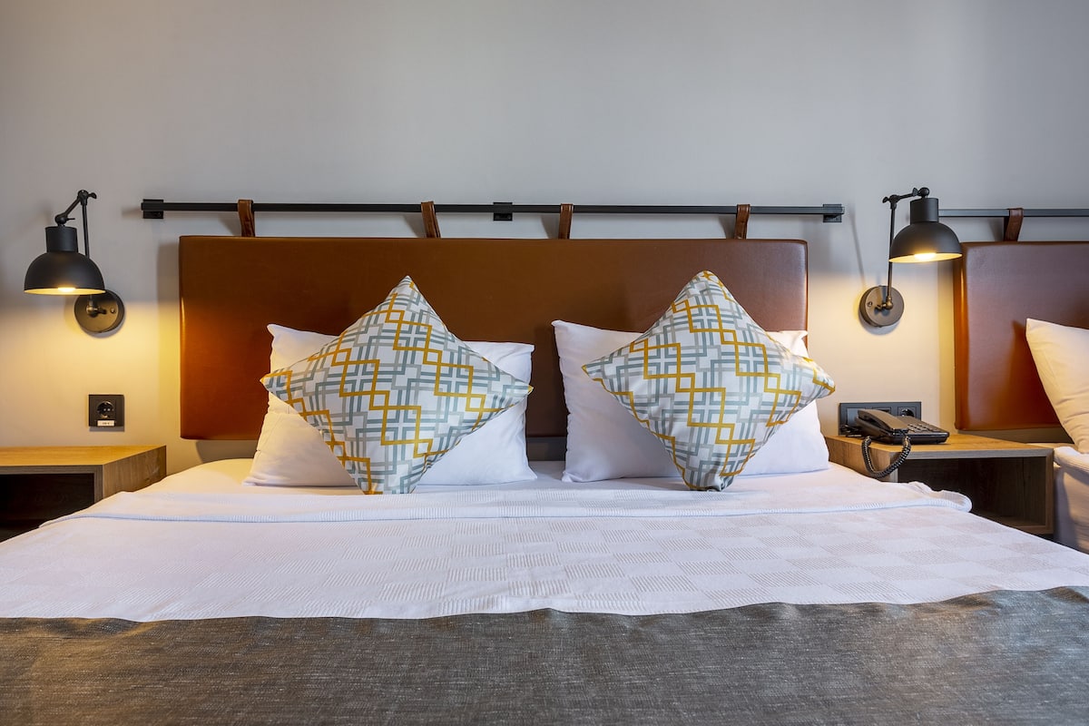 A neatly made bed with patterned pillows, two bedside lamps, and a bedside phone on a wooden nightstand.
