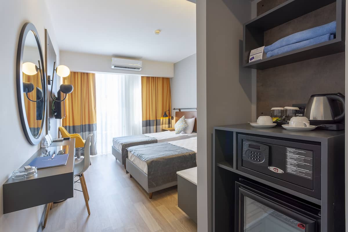 A hotel room with a desk, two beds, a mirror, a coffee maker, and a microwave.