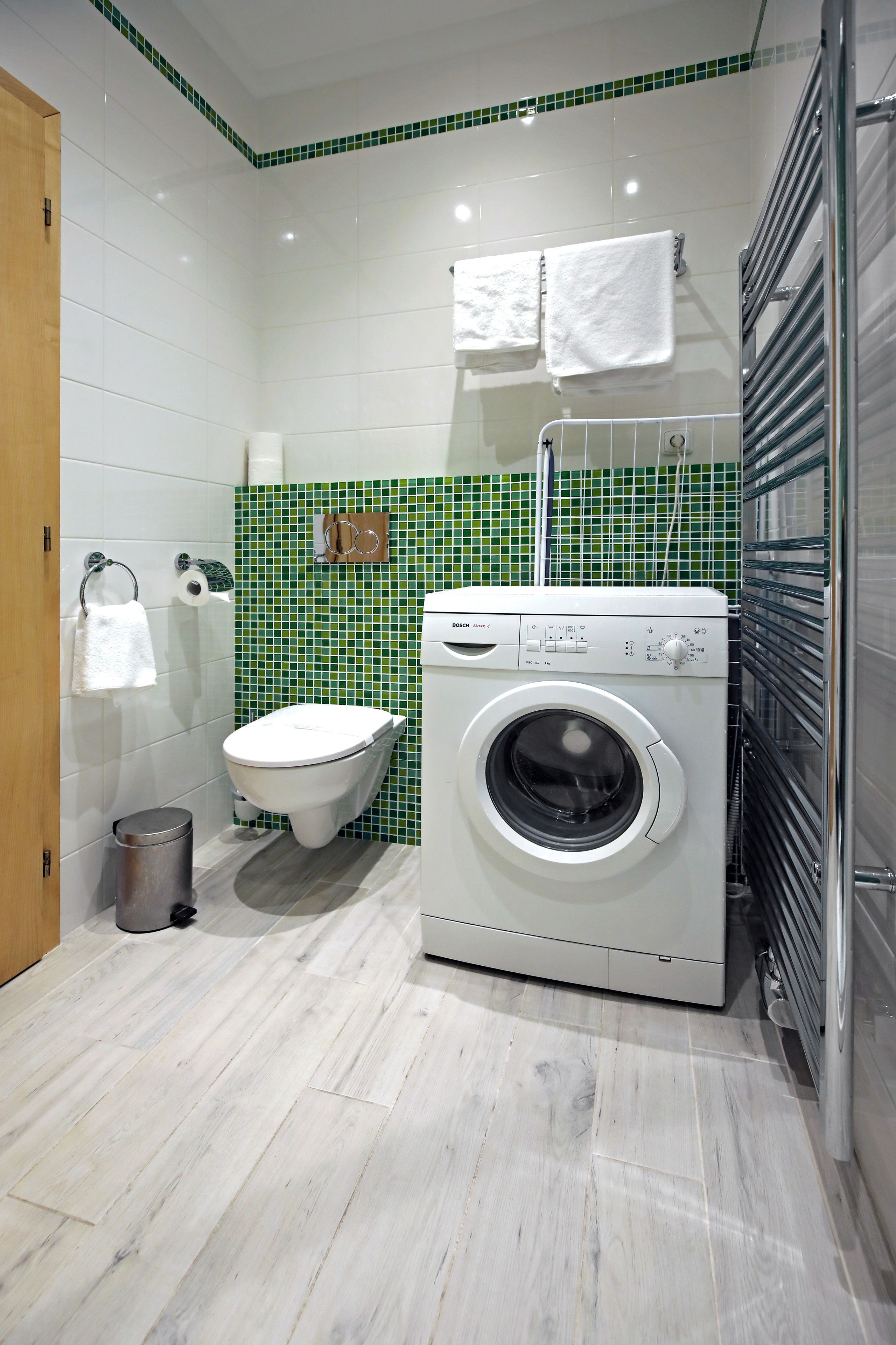 A compact bathroom with a white toilet, a washing machine, and a tiled backsplash.