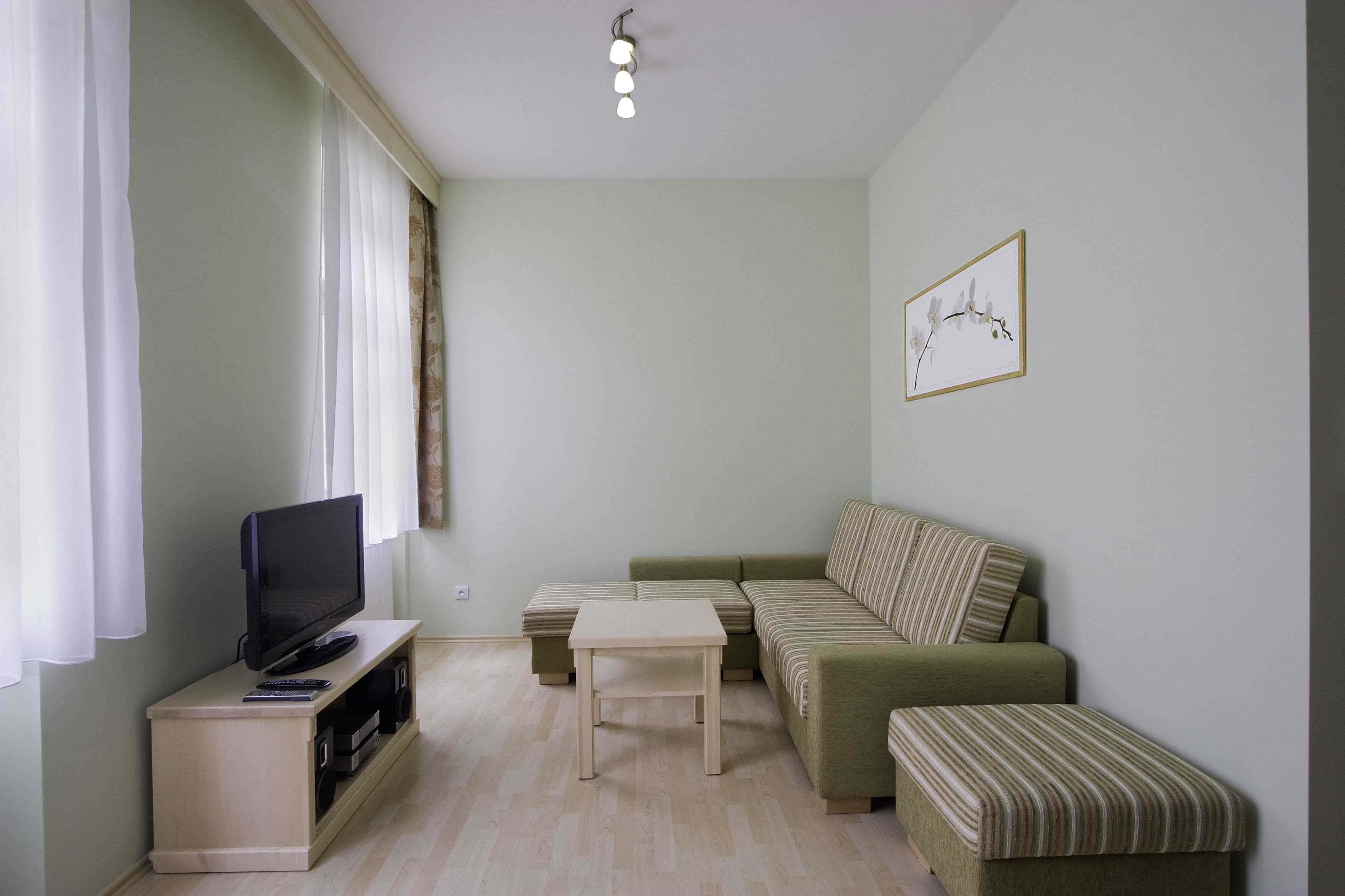 Una sala de estar con televisor de pantalla plana, un sofá, una mesita de centro y una mesa pequeña.