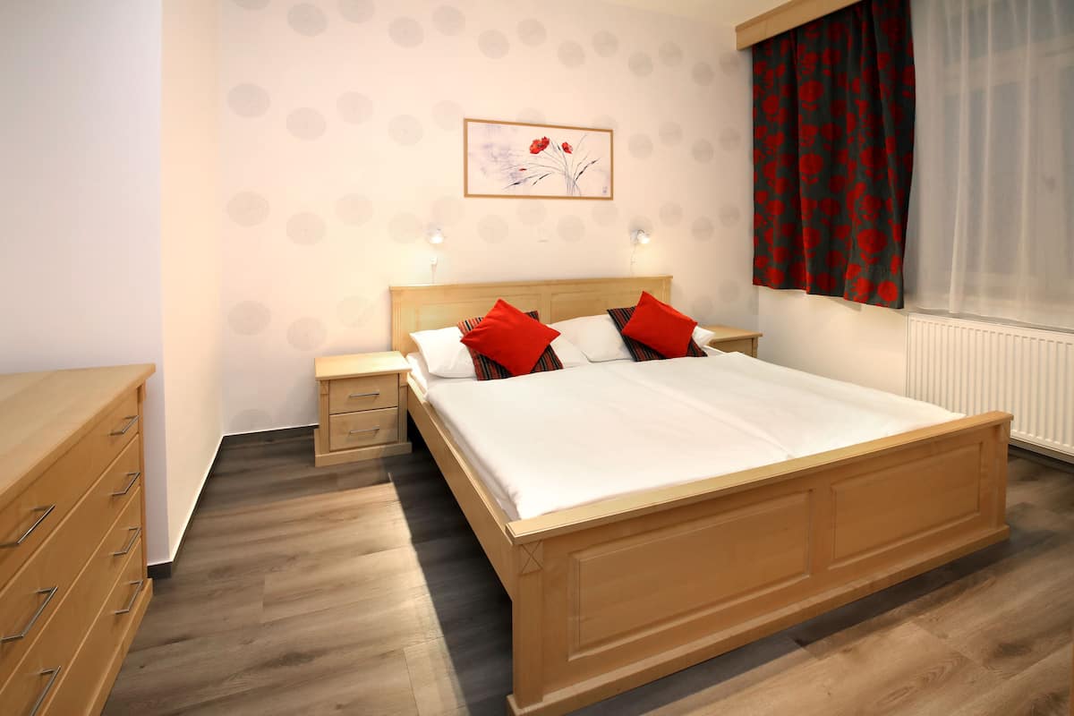 A bedroom with a wooden bed, two bedside tables, a nightstand, a dresser, and a window with red curtains.