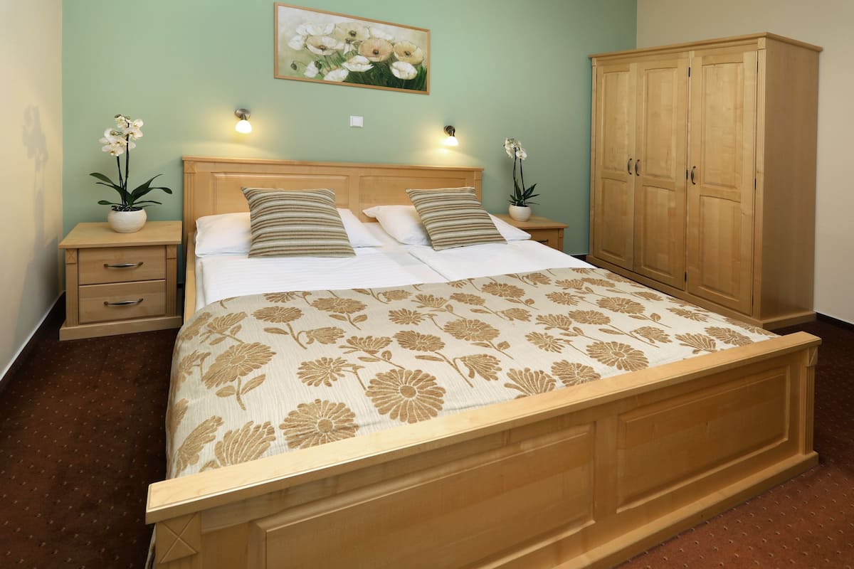 A bedroom with a wooden bed, two nightstands, a wardrobe, and a floral painting on the wall.