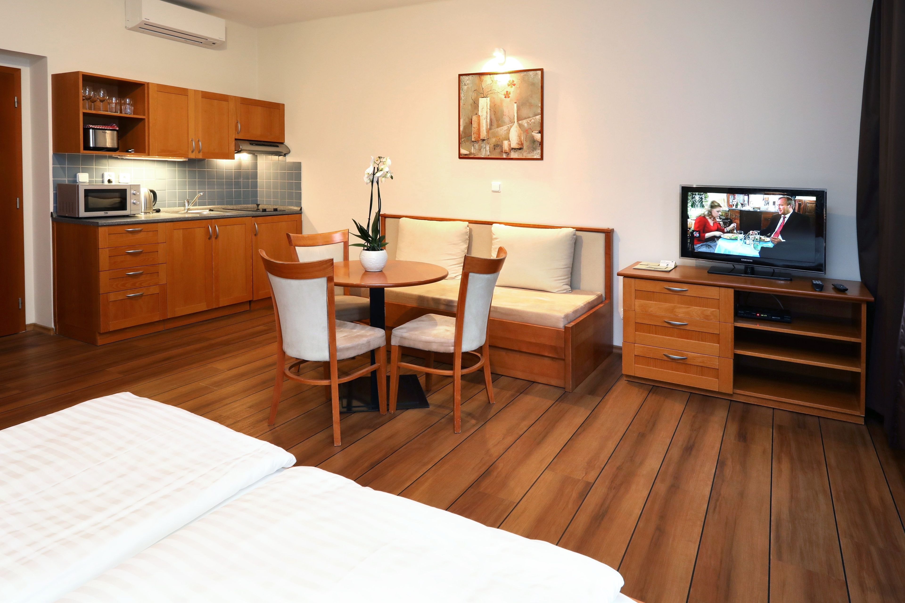 Una moderna camera d'albergo con pavimento in legno, un'area pranzo con tavolo e sedie, un divano, una TV e angolo cottura.