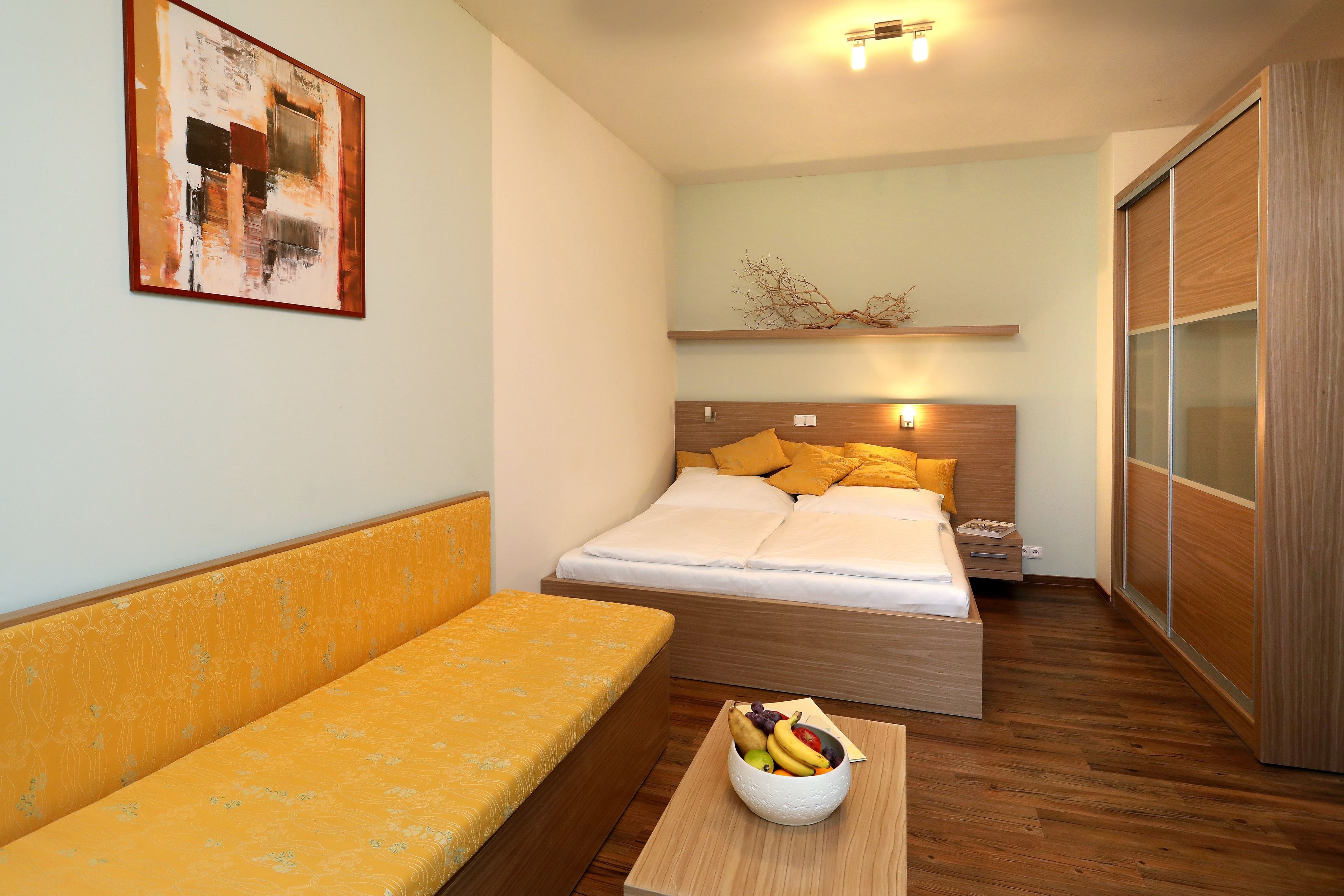 Ein modernes Hotelzimmer mit einem Bett, einer Couch, einem Nachttisch mit Obst und einem an der Wand hängenden Kunstwerk.