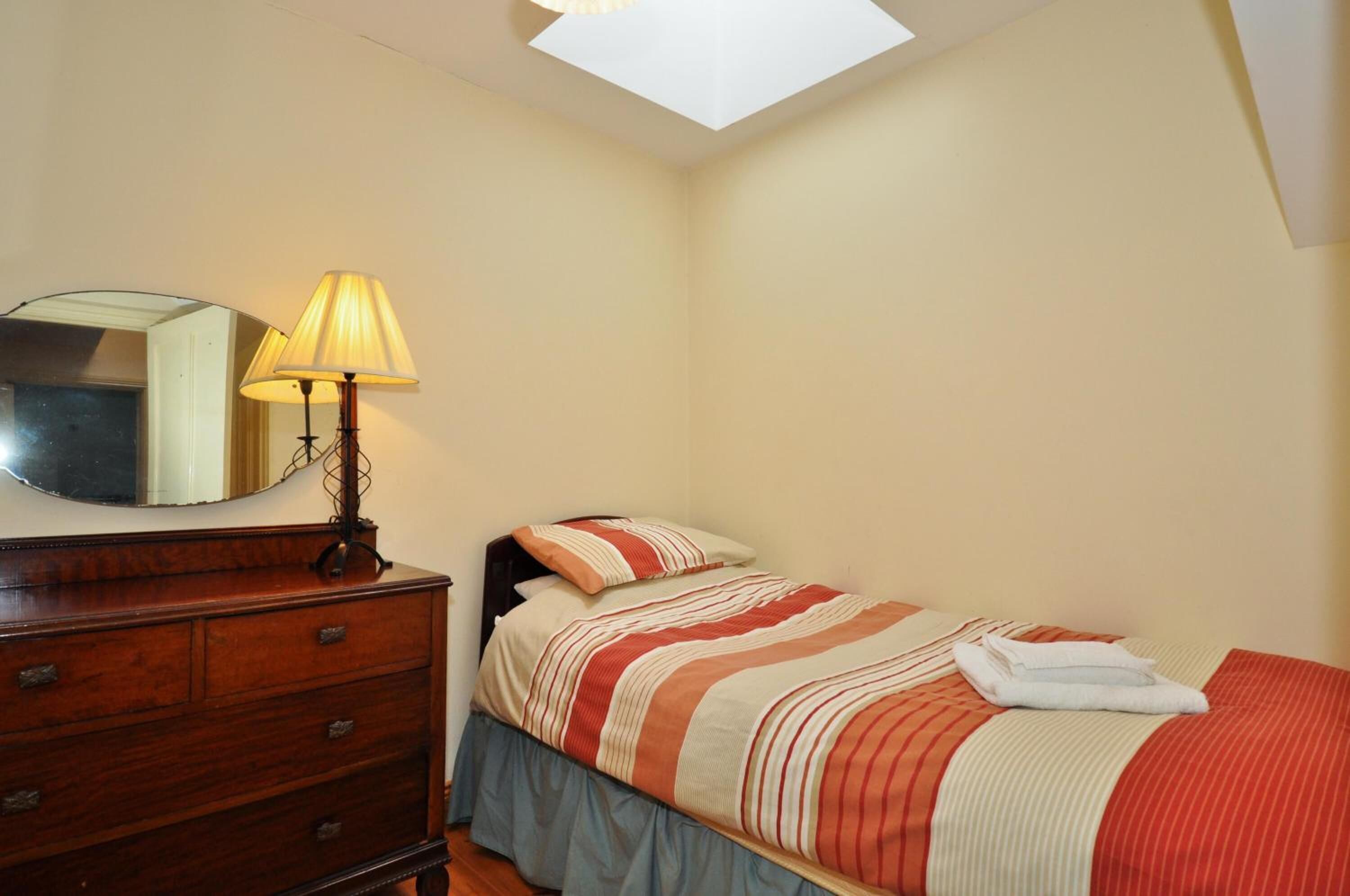 Un dormitorio con cama, cómoda, lámpara y tragaluz.