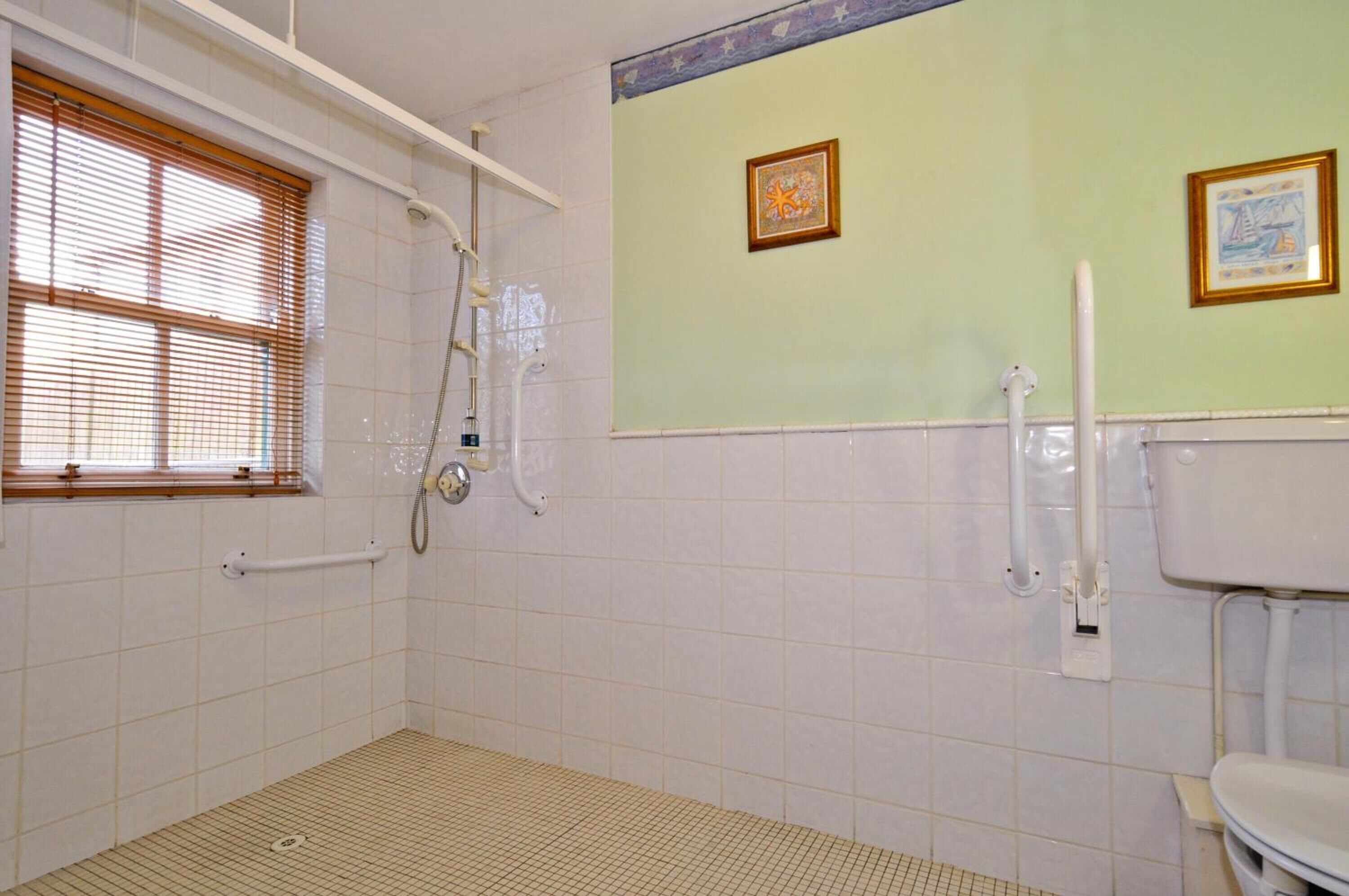 A bathroom with a shower, toilet, and window with blinds.