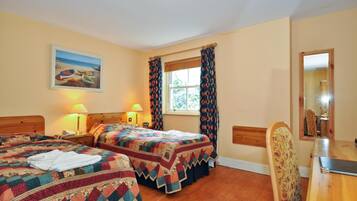Une chambre d’hôtel avec deux lits, une tête de lit en bois, une fenêtre avec des rideaux, un tableau au mur et une table à manger en bois avec une chaise.