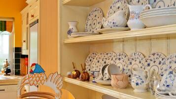 Een keuken met planken vol wit- en blauw gemêleerd servies, een houten stoel en een kleurrijke geruite mat.