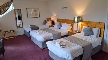 Habitación de hotel con tres camas, cabecera de madera, espejo, cuadro enmarco y alfombra roja.