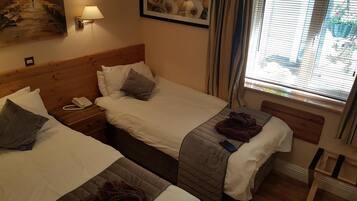 A hotel room with two beds, a bedside table with a phone, a lamp, and a window with curtains.
