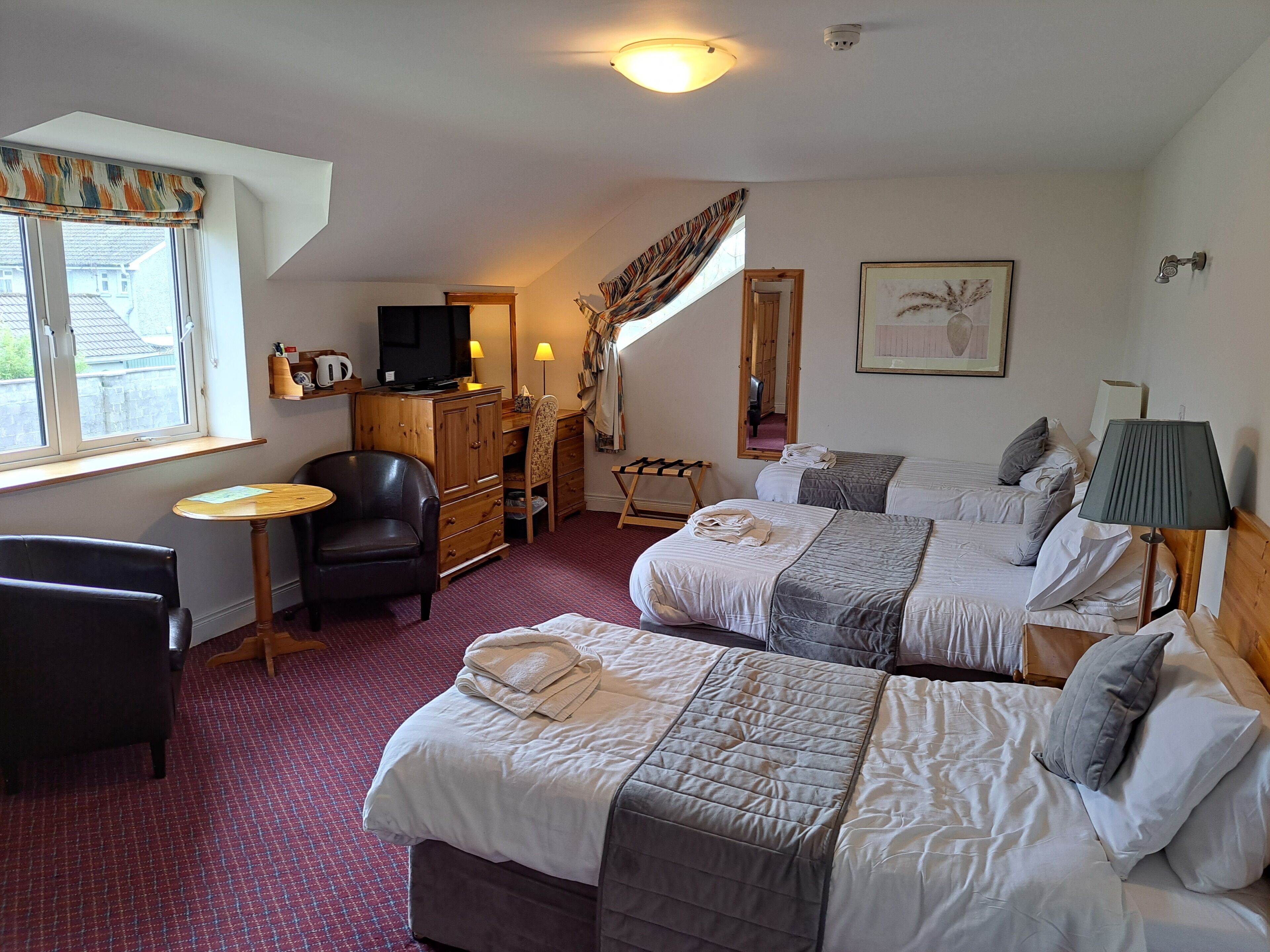 A hotel room with two beds, a desk, a chair, a TV, and a window with curtains.