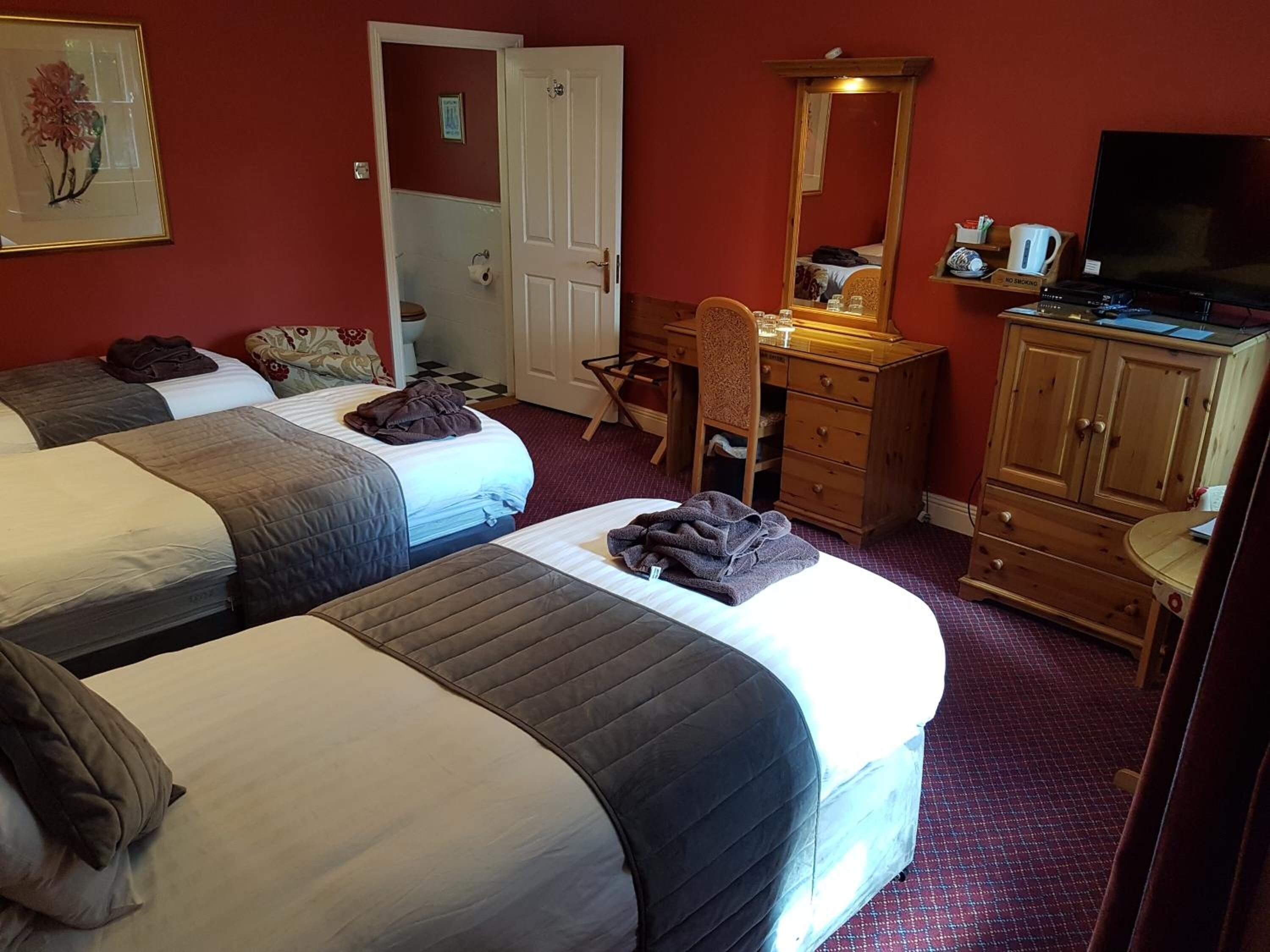 A hotel room with two beds, a desk, a dresser, a mirror, and a television.