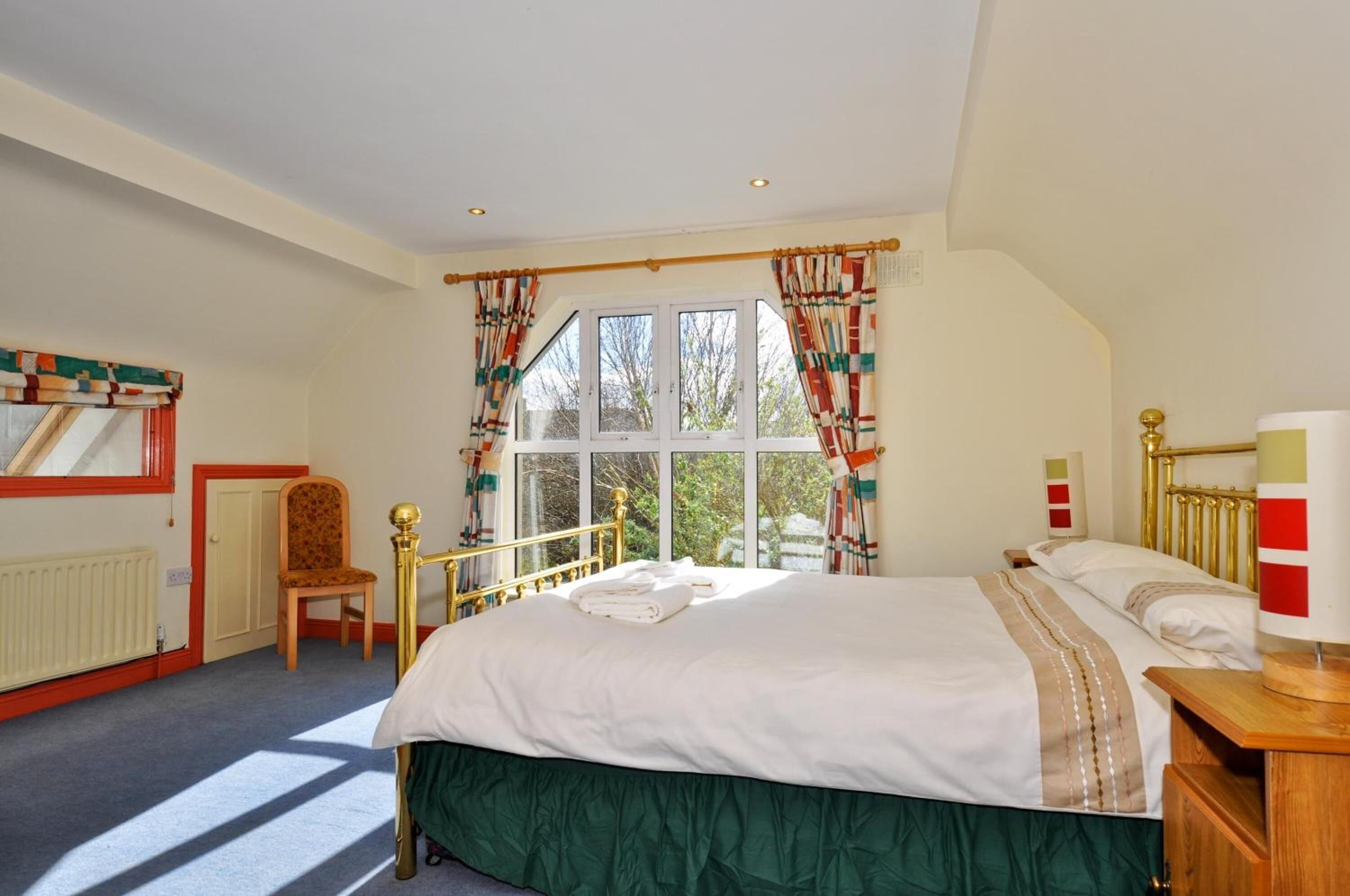 A bedroom with a large bed, a chair, a window with curtains, and a radiator.
