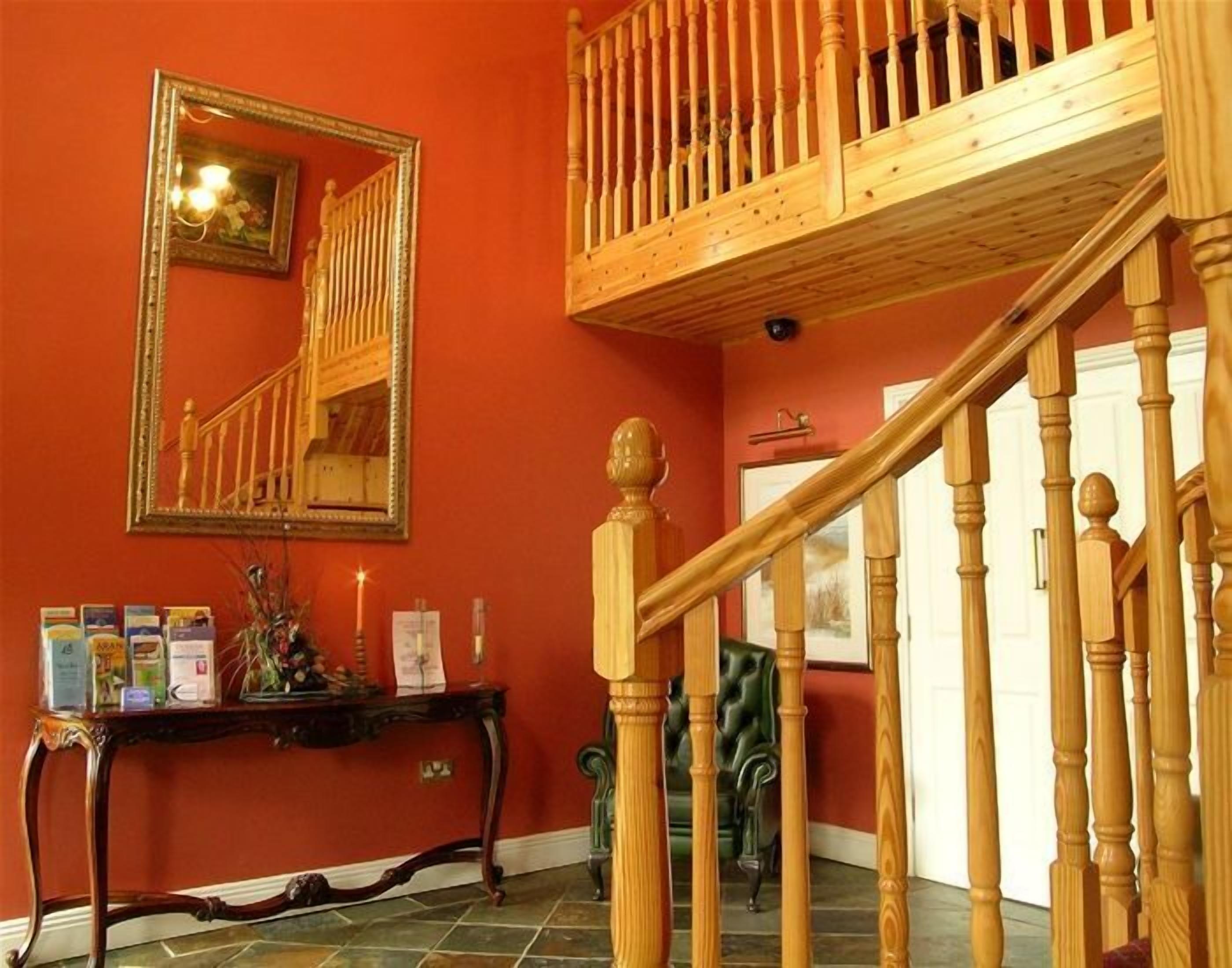 A staircase with wooden balusters and a handrail, leading to an upper floor. A mirror hangs on the wall above the staircase, reflecting part of the room.
