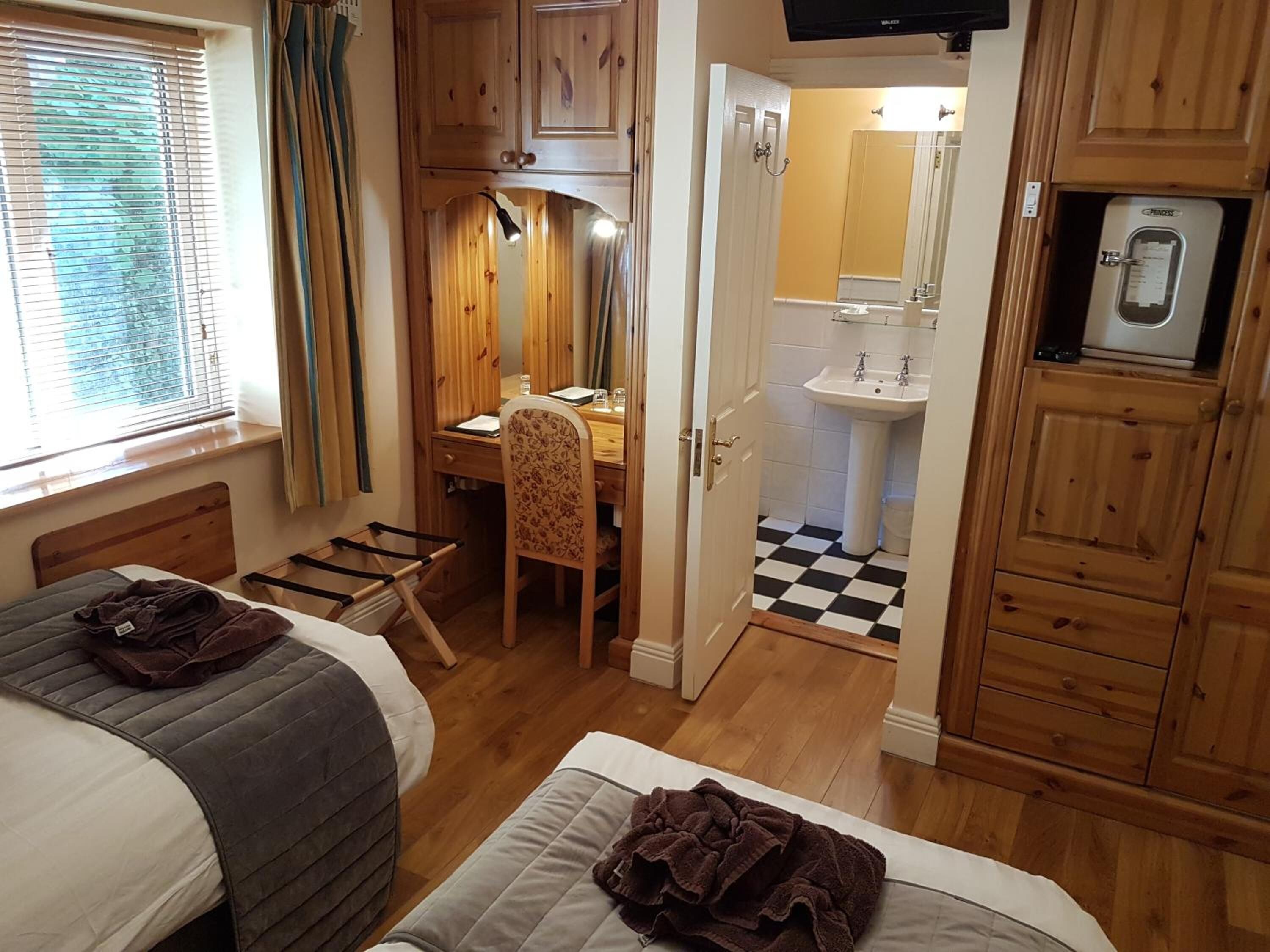 Ein Zimmer mit zwei Betten, einem Schreibtisch, einem Stuhl, einem Waschbecken und einem Fernseher.