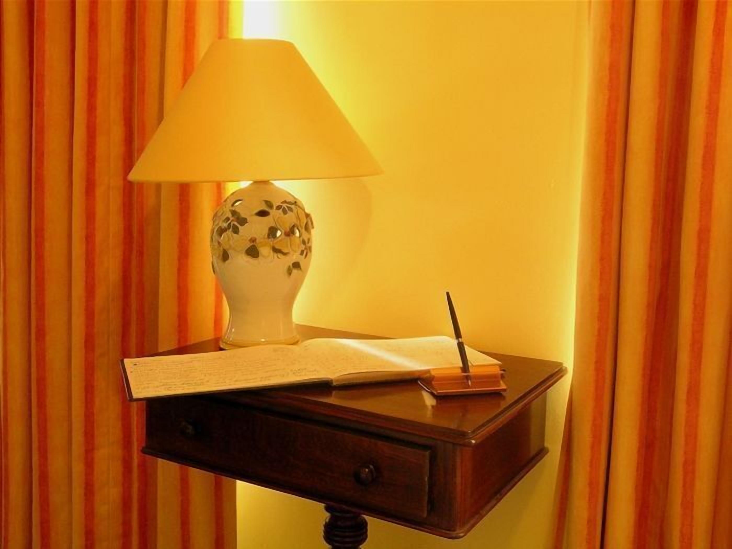 A wooden nightstand with a lamp, a book, and a notepad.