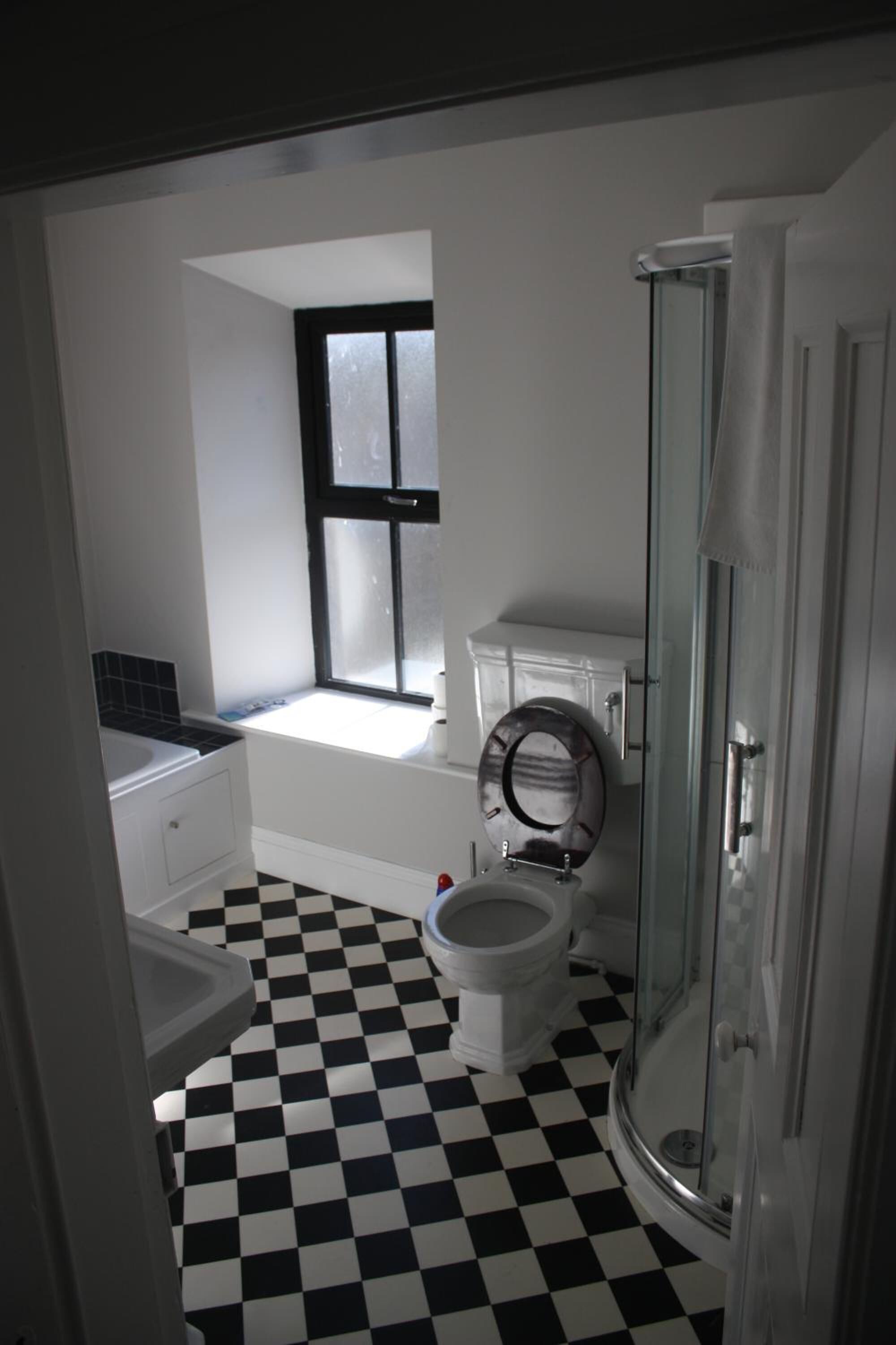 Un baño con suelo a cuadros blanco y negro, un inodoro, una bañera y un box de ducha de vidrio.