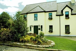 A two-story building with a green door and windows, surrounded by a well-maintained garden with various plants and a wooden bench. - Boffin Lodge (Westport)