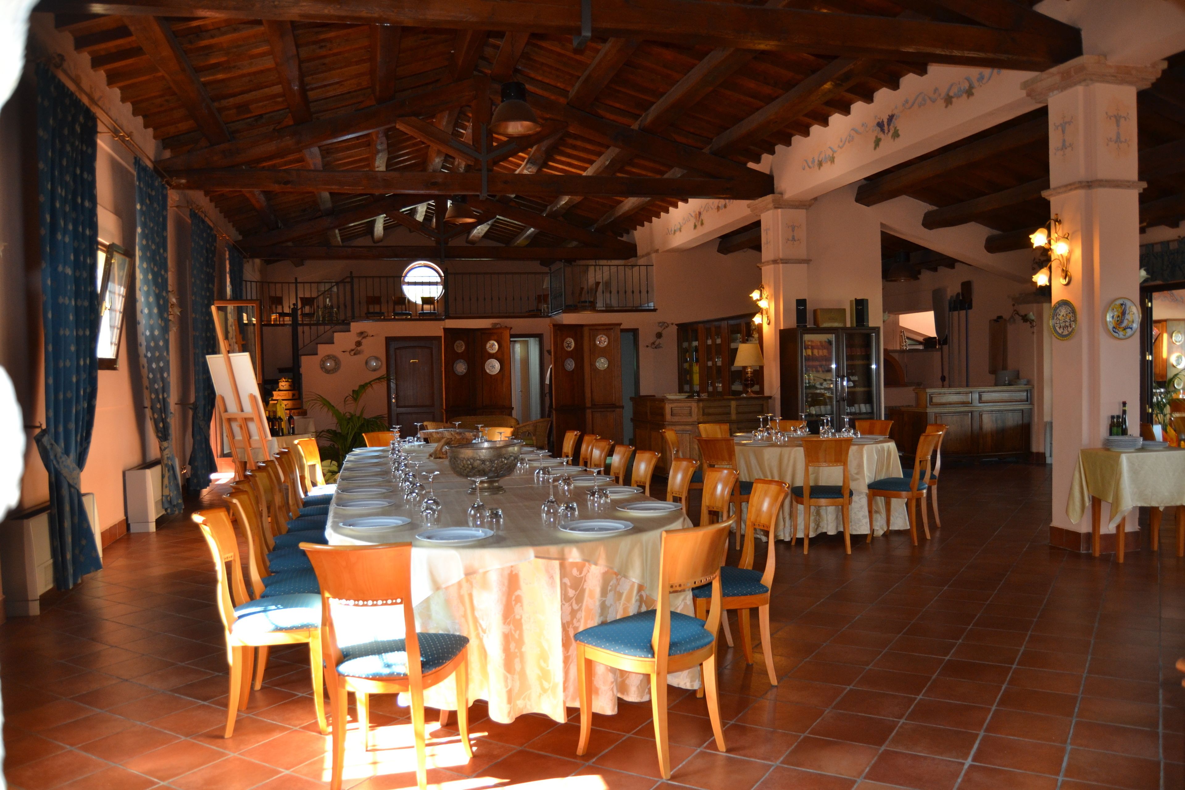 Un comedor espacioso con techo alto y vigas de madera, con una mesa larga dispuesta para una comida, rodeada de sillas de madera con cojines azules.