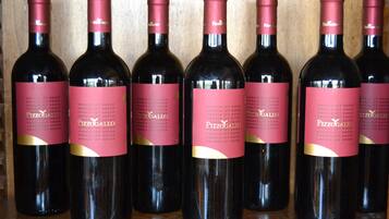 Six wine bottles with pink labels and gold accents, arranged in a row on a wooden surface.