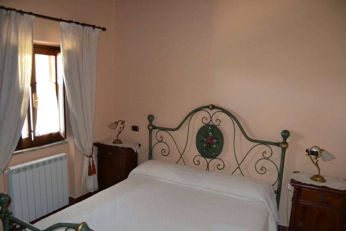 A bedroom with a bed, a nightstand, a dresser, a radiator, and a window with curtains.