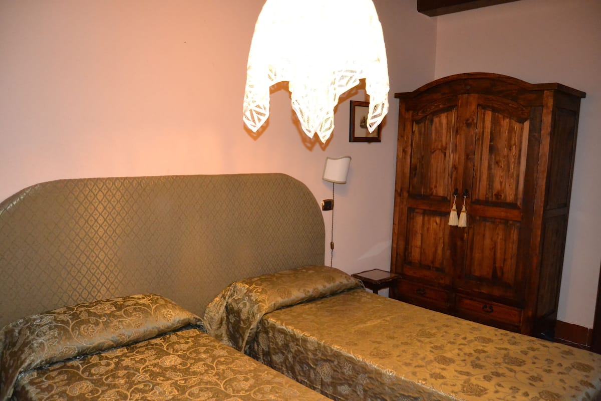 A bedroom with a bed, a wooden wardrobe, and a wall-mounted lamp.