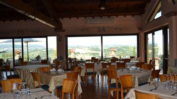 Un restaurante con varias mesas dispuestas para comer, amplios ventanales que ofrecen vistas al campo y un techo de madera.