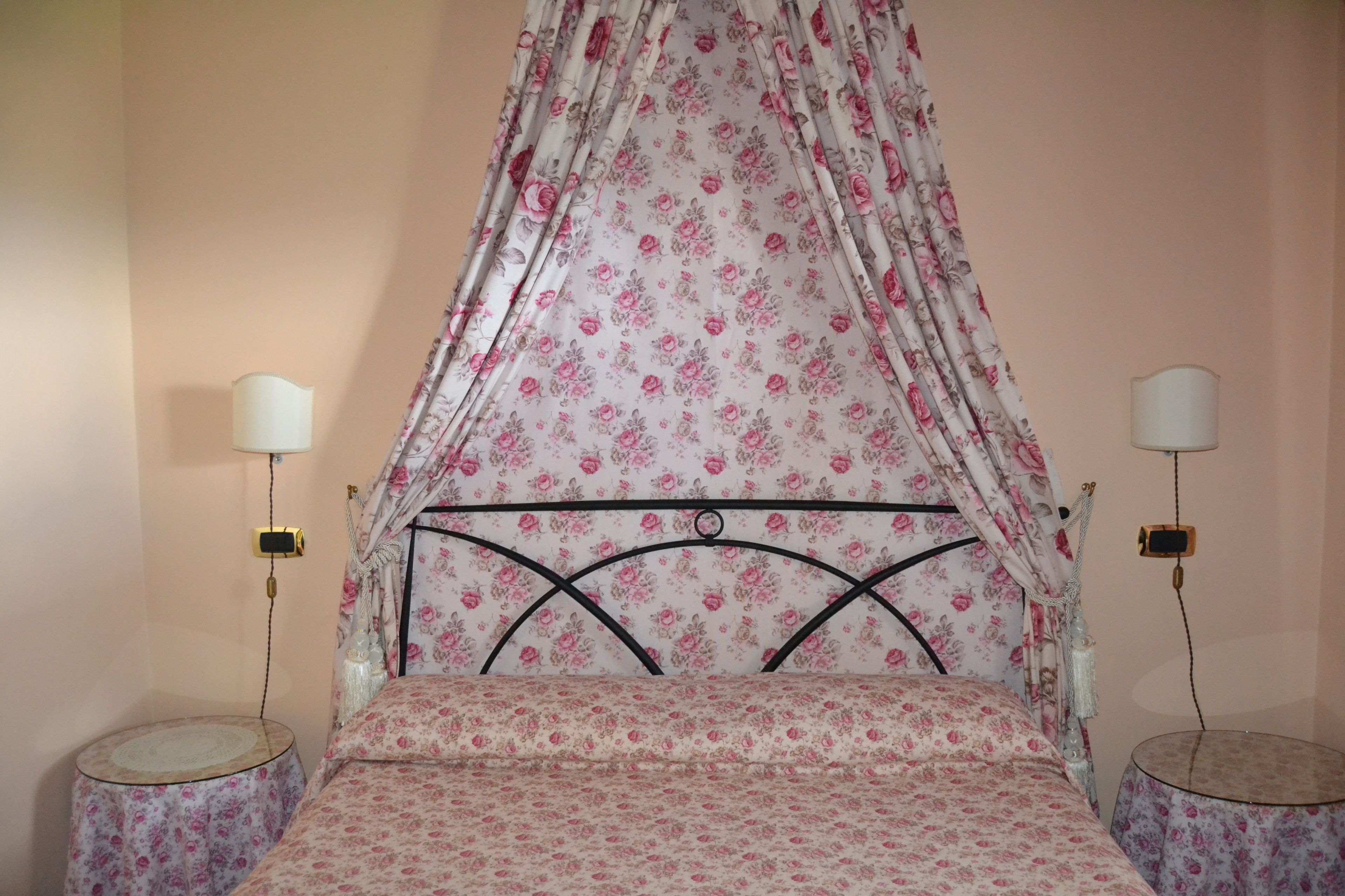 A bedroom with a canopy bed, two bedside tables, and a wall-mounted lamp.